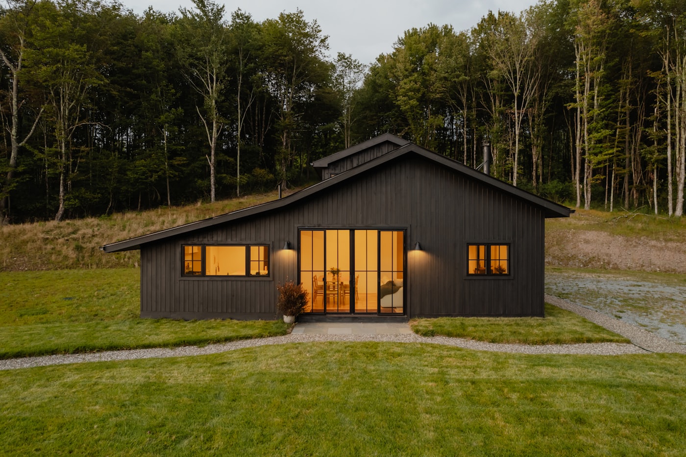 Eco-villa hiện đại với ô kính lớn ánh đèn vàng ấm lúc hoàng hôn, giữa khoảng rừng
