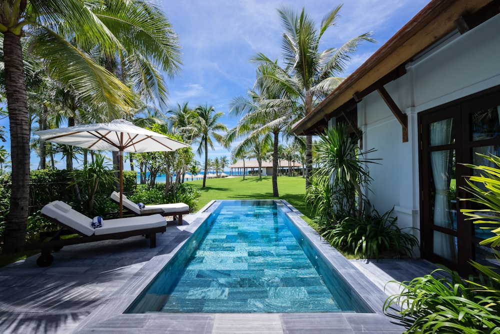 Khu vườn biệt thự rợp bóng dừa với hồ bơi dài dẫn ra biển, ghế tắm nắng và dù trắng