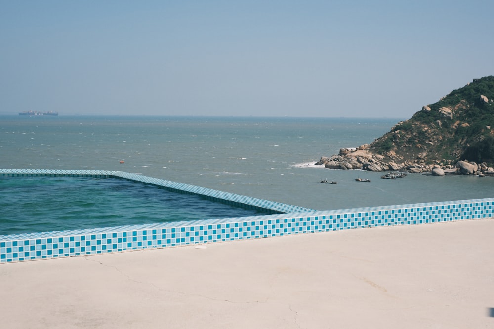 Hồ bơi vô cực viền gạch mosaic xanh nhìn thẳng ra biển khơi và mỏm đá